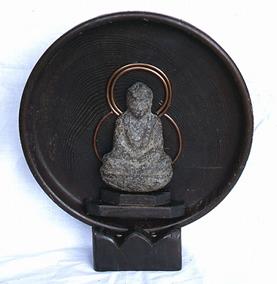 黒い円形の円の中に石のようなもので作られている如来形坐像が作られている鉄鋳如来形坐像の写真