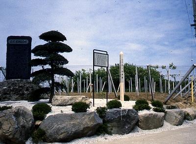 岩で囲まれた一角に松の木が生えており、黒く大きい石碑と案内版が立っている、日ノ出城跡に立つ石碑の写真