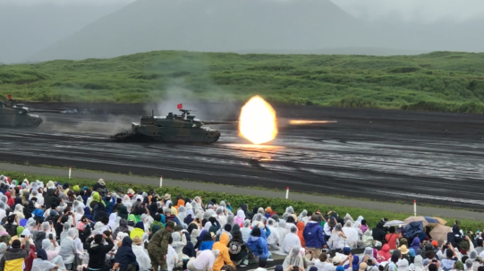 戦車から火が出ている様子を多くの人が見物している写真