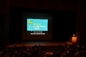 ステージ上に「令和がん年度男女共同参画推進委員会活動報告」と映し出されたプロジェクタースクリーンがありステージの右端でマイクに向かって話しをしている写真