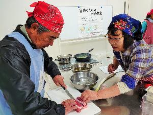 中年男性が肉を切るのを中年女性が補助している写真