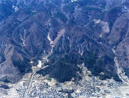 山脈と白山城跡の麓に田畑と住宅が広がっている様子を上空か映している写真