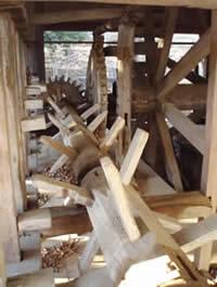 横たわった木製の柱のような杵の先端に歯車が設置されている様子の写真
