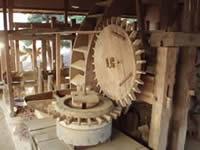 石臼の上に木製の歯車が乗っており、石臼の上の歯車と噛み合うように石臼の横に大きな木製の歯車が設置されている写真