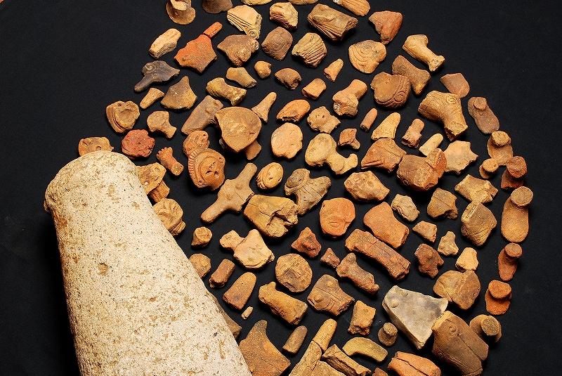 女夫石遺跡から発見された人の顔や体の形をした土偶や模様が刻まれている土器のかけらが沢山並べられている写真