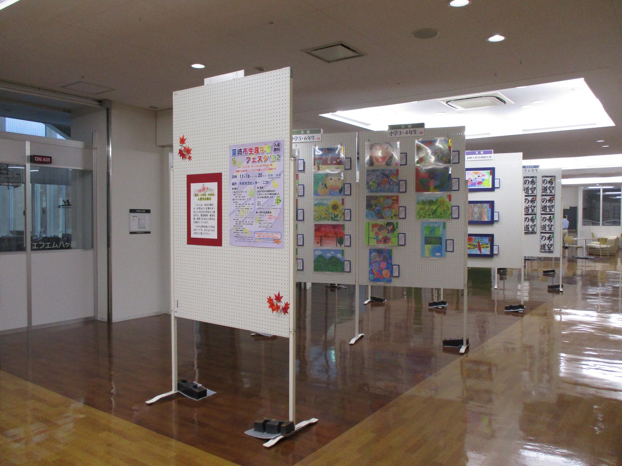 ニコリイベントスペースに児童の絵画や習字などの作品が展示されている様子の写真