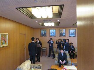 韮崎市長特別表彰が行われており、男性が市長より表彰を受けている様子を複数のカメラが撮影をしている様子を写している写真