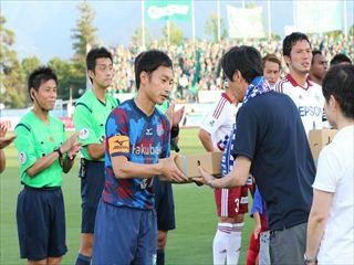 試合前のセレモニーで市長が選手の代表の方に箱に入った桃を贈呈している様子の写真