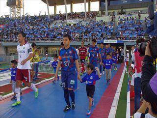 ヴァンフォーレ甲府と相手チームが試合会場のグラウンドにエスコートキッズの子ども達と手をつないで入場している様子の写真