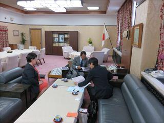 応接室の中央の席に麻生 太郎 副総理が座っており、左側に赤いワンピースを着た女が座っており、右側のに座っている男性と麻生 太郎 副総理が資料をひろげて、興味深く見ている様子の写真