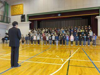 体育館で北東小学校の6年生が市長の前で合唱を披露している写真