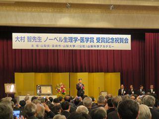 大村智先生ノーベル生理学・医学賞受賞記念祝賀会で、話をする男性の写真