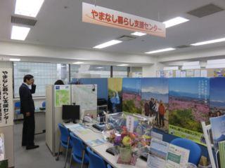事務所の中に並んだ机の上に花が飾ってあり、奥に職員が立っている写真