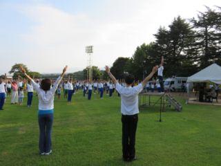 参加者たちが立って両手を斜め上に伸ばして体操をしている写真