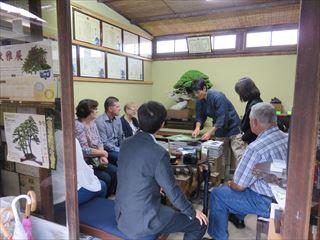 盆栽園の室内で、着席している親善使節団の方々と市長の前で話をしている男性の写真