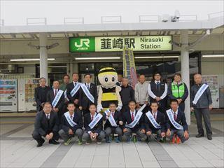 韮崎駅前で、タスキをして整列する関係者や、甲府税務署の副署長さんや韮崎高校野球部の生徒の集合写真
