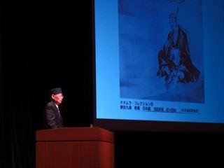 大村 智博士が壇上にて、映像を見ながら講演をしている様子の写真