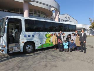 ニーラのキャラクターが描かれている新しいスクールバスの前で子ども達と関係者が一緒に移っている写真