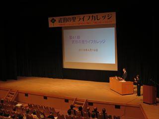 「武田の里ライフカレッジ」の開講式で、市長が壇上にて映像を映しながら、講演をしている様子の写真