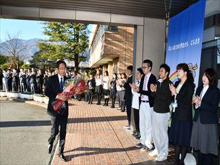 市長が花束をもって市役所の玄関前を歩いており、職員の皆様が拍手をして出迎えている様子の写真