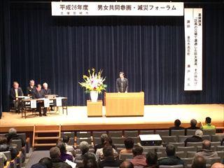 「平成26年度 男女共同参画・減災フォーラム」の横断幕の前で市長が講壇に立ち話をしており、沢山の来場者が話を聞いている様子の写真