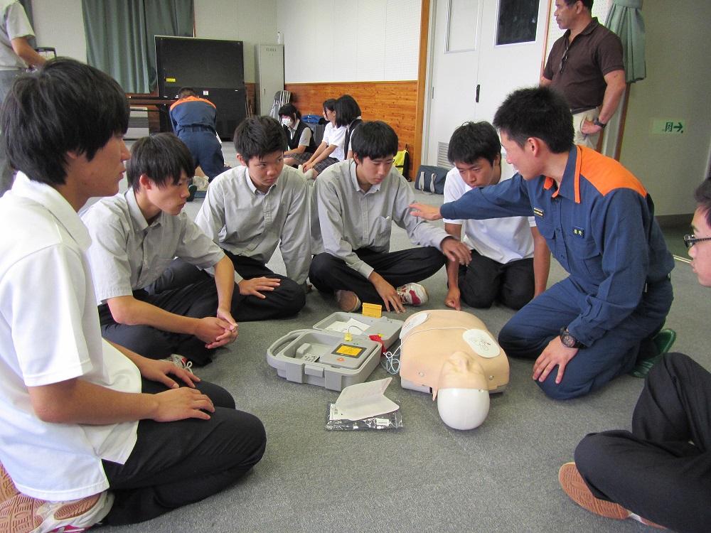 男子学生5名に救命士が人体モデルとAEDを床において説明している様子の写真
