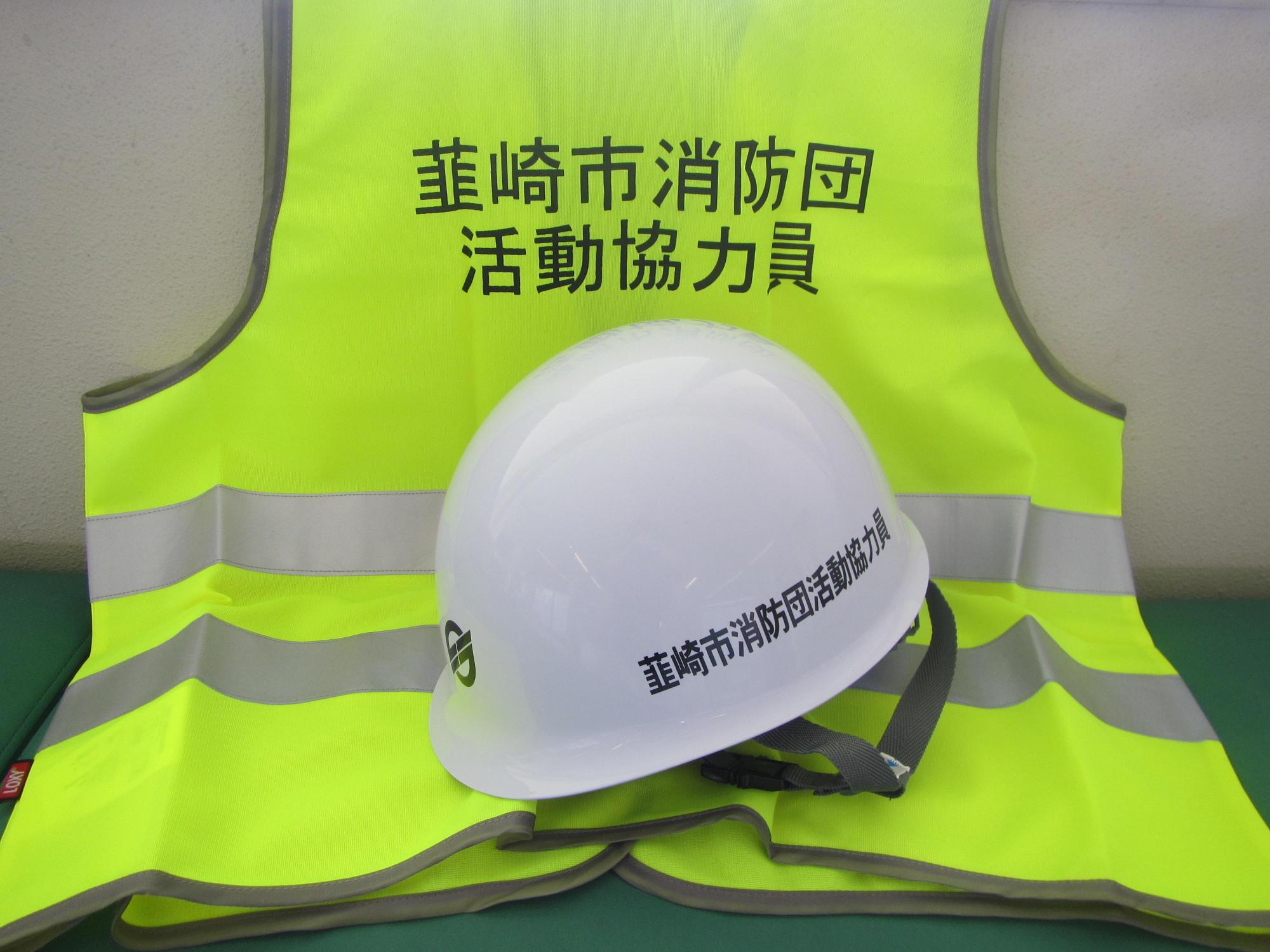 韮崎市消防団活動協力員と記載のある緑色の蛍光色のベストの上に白いヘルメットを置いた写真