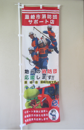 韮崎市消防団サポート店 地元の消防団応援します!!と書かれてありニーらが放水持ち消防車の前に立っている写真と消防団員が写っているのぼりの写真