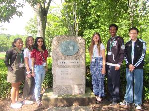 6名の高校生が中央公園にある喜恵子・ウィタカーの碑の周りにたって撮影した記念写真