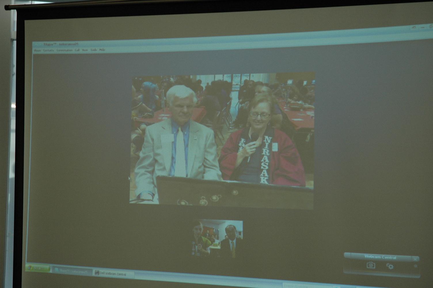 スクリーンに映し出された白髪のフェアフィールド市長と赤色のはっぴを着たフェアフィールド姉妹都市実行委員会長の写真