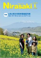 奥には山が見えていて、手前の菜の花畑に赤ちゃんを抱っこした男性と、その横に女性二人と男の子が立っている姿が写っている広報にらさき6月号表紙