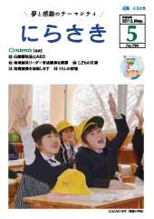 教室の机に座っている黄色い帽子を被った新一年生が笑顔で手を挙げている写真が載っている広報にらさき5月号表紙