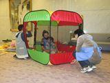 託児所の職員が、緑色と赤色の正方形の形をしたテントの中で子供と遊んでいる写真
